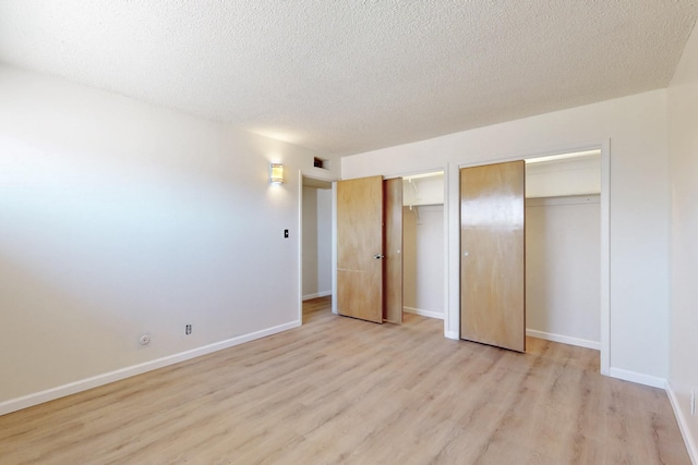 unfurnished bedroom featuring visible vents, two closets, light wood-style flooring, a textured ceiling, and baseboards