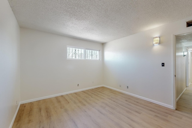 spare room with light wood finished floors, a textured ceiling, and baseboards