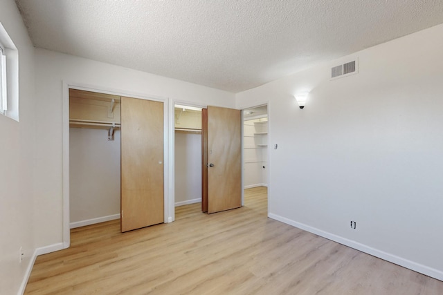 unfurnished bedroom featuring visible vents, light wood-style flooring, a textured ceiling, and baseboards