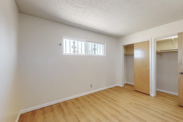 unfurnished bedroom with baseboards, two closets, and wood finished floors