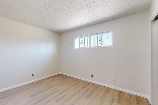 unfurnished room featuring baseboards, light wood finished floors, and a textured ceiling