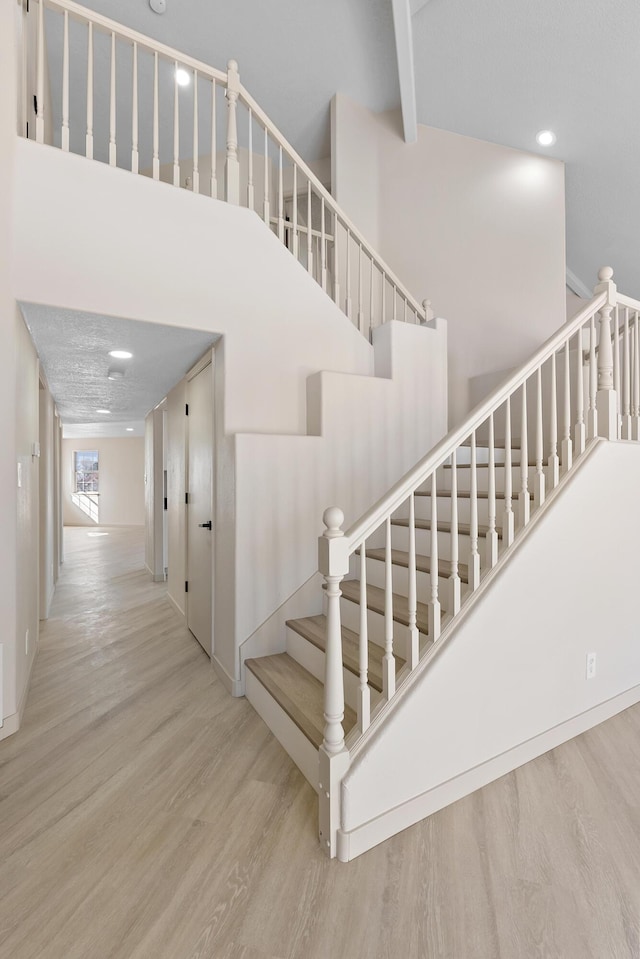 stairs featuring beamed ceiling, a high ceiling, and wood finished floors