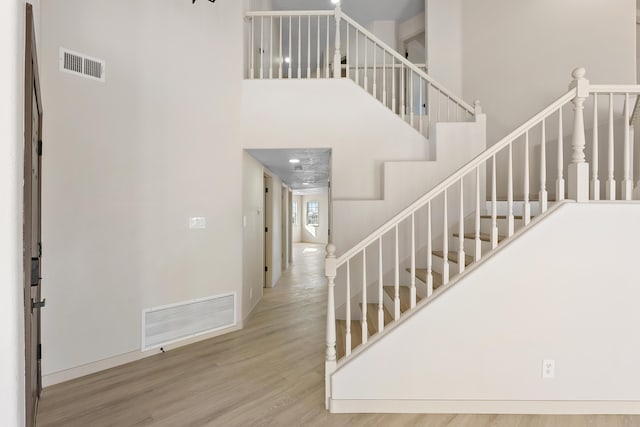 staircase with a high ceiling, wood finished floors, and visible vents