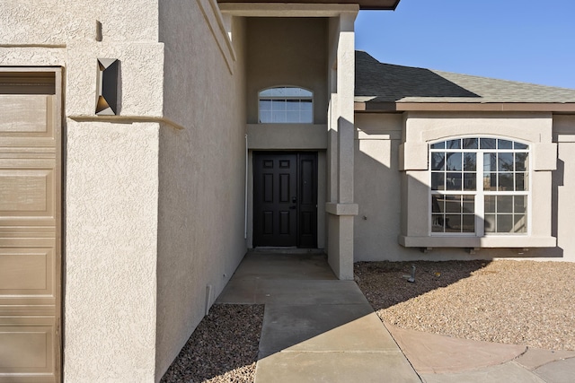 property entrance with stucco siding, a shingled roof, and a garage