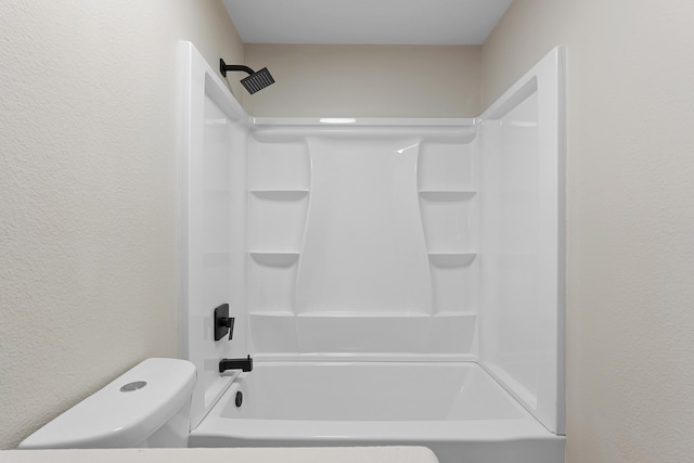 bathroom featuring shower / bathing tub combination, toilet, and a textured wall