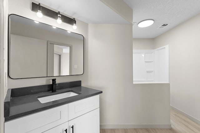 full bath featuring visible vents, a textured ceiling, wood finished floors, baseboards, and vanity