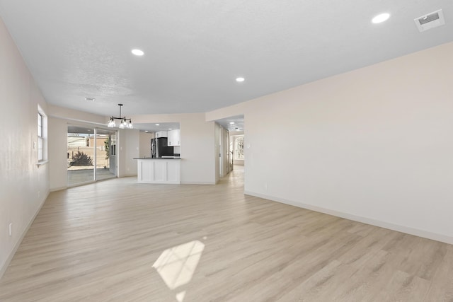 unfurnished living room featuring visible vents, baseboards, an inviting chandelier, light wood-style flooring, and recessed lighting