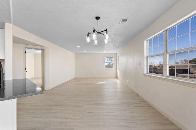 interior space featuring light wood finished floors, visible vents, baseboards, a notable chandelier, and a textured ceiling