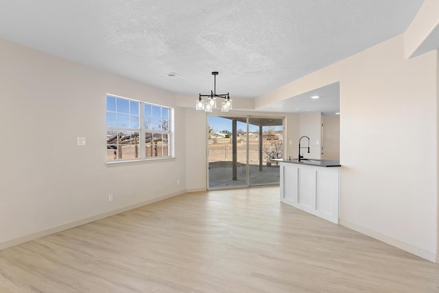 unfurnished living room with a chandelier, light wood finished floors, a textured ceiling, and baseboards