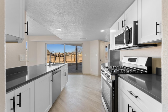 kitchen featuring a sink, stainless steel appliances, dark countertops, and white cabinetry