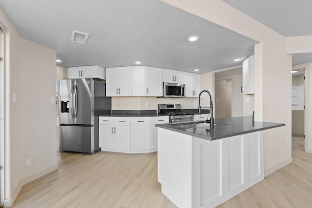 kitchen featuring visible vents, light wood-style flooring, a sink, dark countertops, and appliances with stainless steel finishes