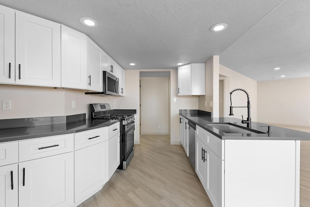 kitchen with light wood-type flooring, a sink, dark countertops, appliances with stainless steel finishes, and white cabinets