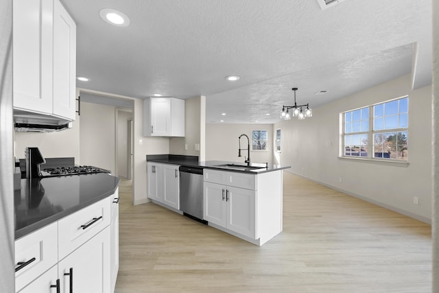 kitchen with dark countertops, a peninsula, stainless steel dishwasher, white cabinetry, and a sink