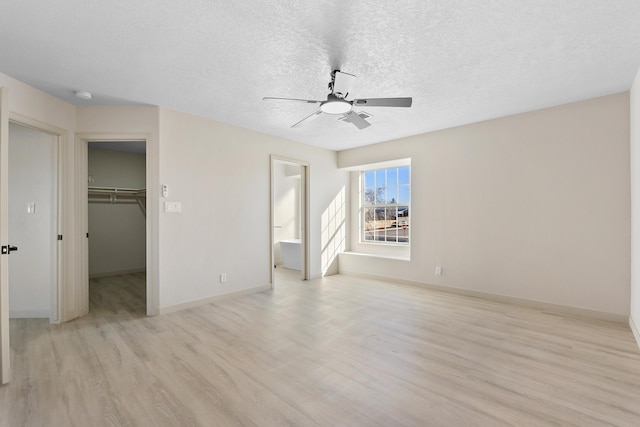 unfurnished bedroom featuring a walk in closet, a ceiling fan, a textured ceiling, light wood-style floors, and baseboards