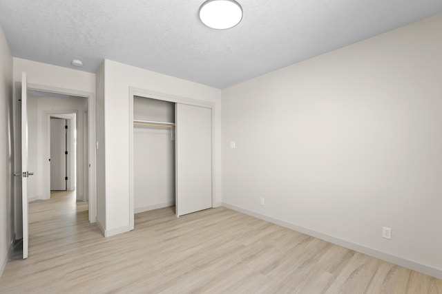 unfurnished bedroom featuring a closet, baseboards, a textured ceiling, and light wood-style flooring