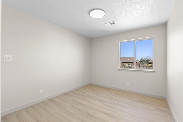 unfurnished room with baseboards, wood finished floors, visible vents, and a textured ceiling