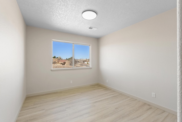 unfurnished room with baseboards, wood finished floors, visible vents, and a textured ceiling