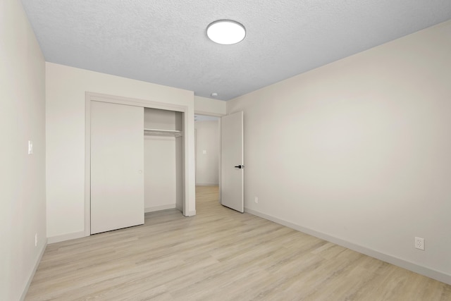 unfurnished bedroom featuring light wood-style flooring, baseboards, a closet, and a textured ceiling