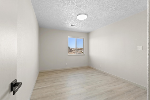 spare room featuring visible vents, baseboards, light wood-style floors, and a textured ceiling