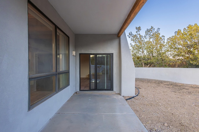 view of exterior entry with stucco siding, a patio, and fence