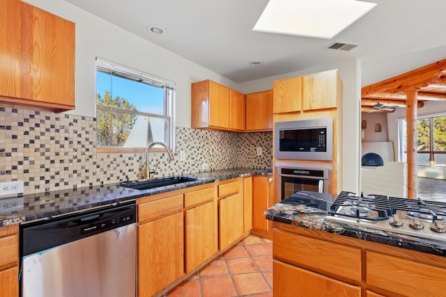 kitchen featuring visible vents, a sink, dark stone countertops, stainless steel appliances, and light tile patterned floors