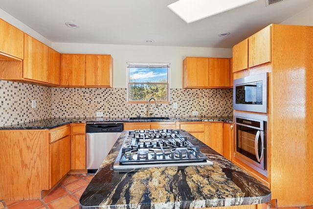 kitchen with light tile patterned floors, a kitchen island, a sink, decorative backsplash, and stainless steel appliances