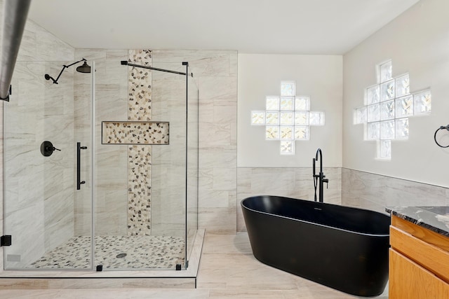 bathroom with a soaking tub, a shower stall, tile walls, and vanity