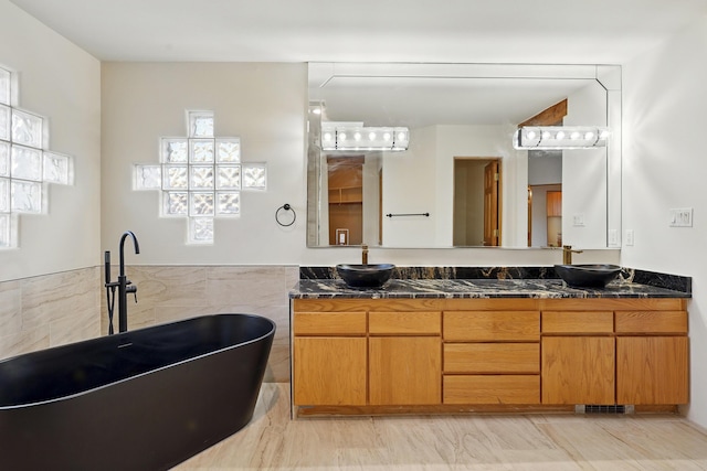 full bathroom featuring double vanity, a soaking tub, tile walls, and a sink