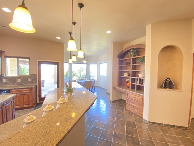 kitchen featuring light stone counters, brown cabinetry, recessed lighting, dark tile patterned floors, and backsplash