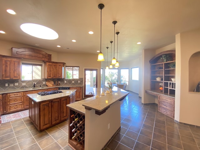 kitchen featuring tasteful backsplash, brown cabinets, black gas cooktop, and a kitchen island with sink