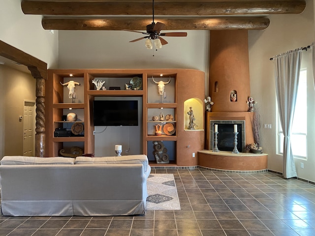 living area featuring beam ceiling, dark tile patterned floors, a ceiling fan, a glass covered fireplace, and baseboards