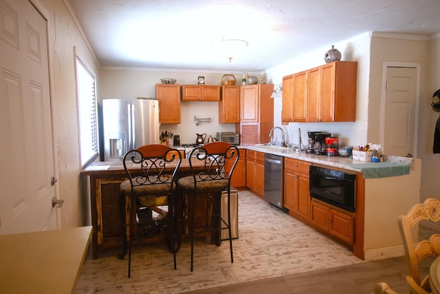 kitchen featuring crown molding, light countertops, light wood-style floors, stainless steel appliances, and a sink