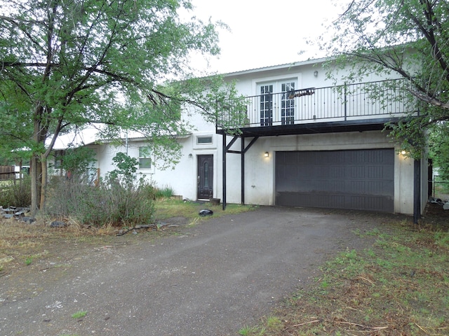 view of front of house featuring a balcony, french doors, driveway, and stucco siding