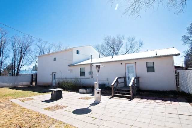 rear view of property featuring metal roof, a fire pit, a patio, and fence