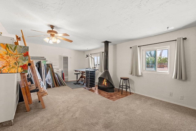 playroom with a ceiling fan, a textured ceiling, carpet, a wood stove, and a textured wall