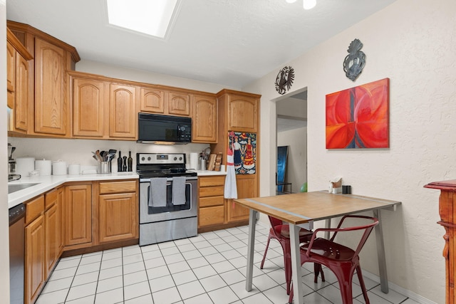 kitchen with appliances with stainless steel finishes, light tile patterned flooring, light countertops, baseboards, and a textured wall