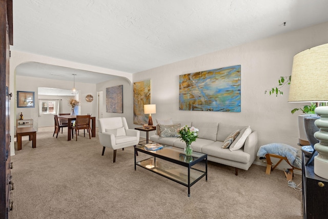 living area with light colored carpet, arched walkways, and a textured ceiling