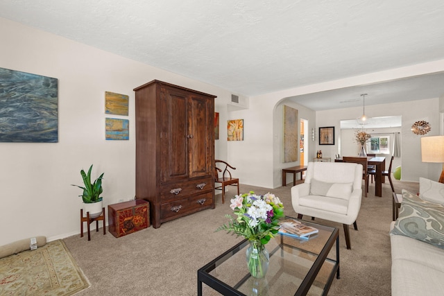 living area with visible vents, arched walkways, light colored carpet, and baseboards