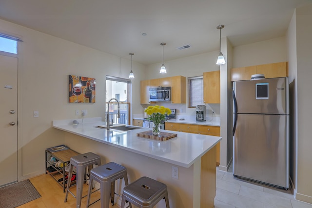 kitchen featuring visible vents, a breakfast bar, light countertops, appliances with stainless steel finishes, and a sink