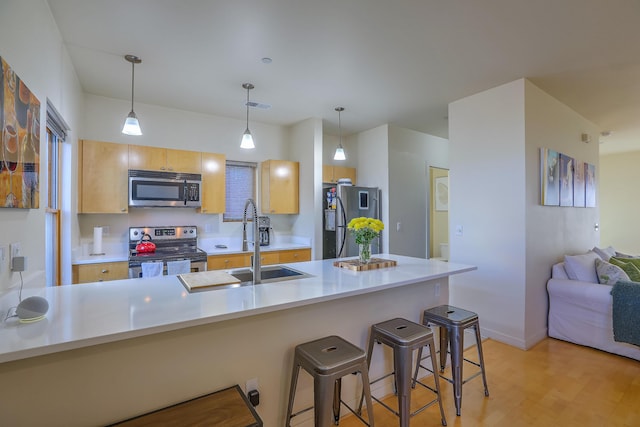 kitchen featuring visible vents, light wood-style flooring, a sink, appliances with stainless steel finishes, and a breakfast bar area