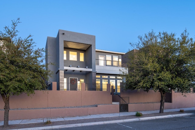 contemporary home with fence, a balcony, and stucco siding