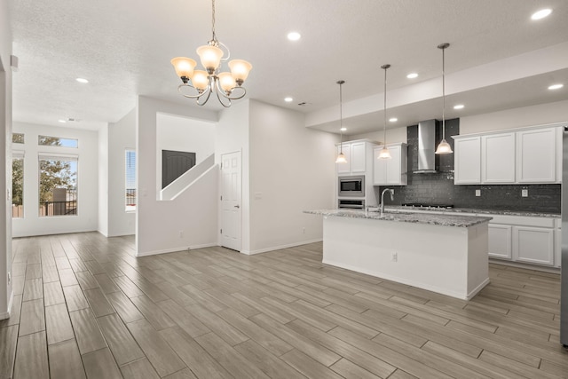 kitchen featuring stainless steel appliances, a center island with sink, tasteful backsplash, recessed lighting, and wall chimney range hood