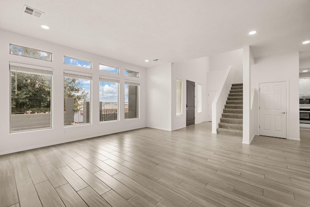 unfurnished living room with light wood-style flooring, visible vents, recessed lighting, and stairway