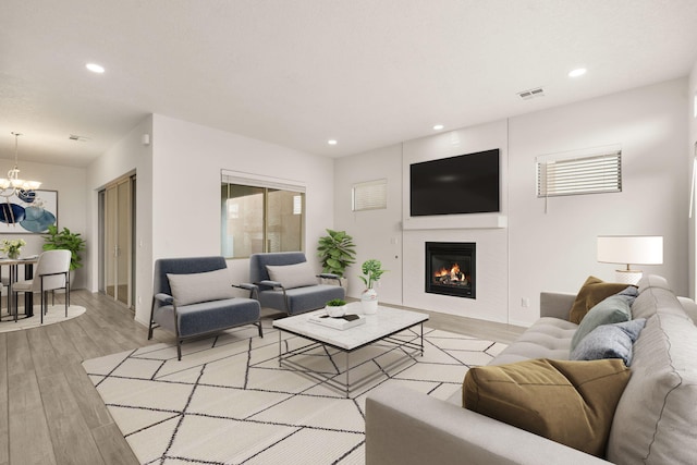 living room featuring recessed lighting, a glass covered fireplace, light wood-type flooring, and a notable chandelier