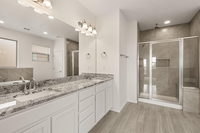 full bathroom featuring a shower stall, wood finished floors, a sink, and double vanity