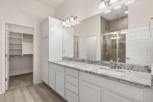 bathroom featuring wood finished floors, a sink, double vanity, and a stall shower