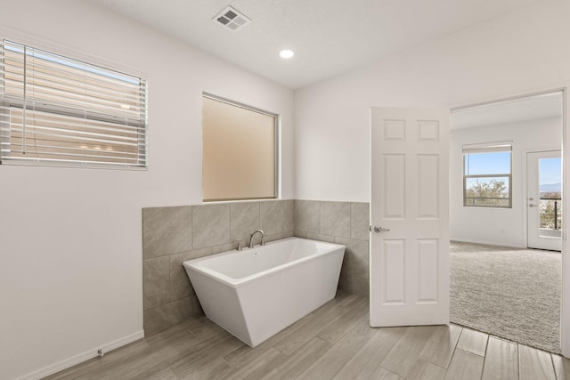 full bath with a freestanding bath, wood finished floors, visible vents, and tile walls