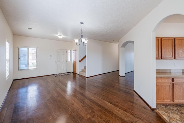 unfurnished dining area featuring dark wood-style floors, a chandelier, arched walkways, and a textured ceiling