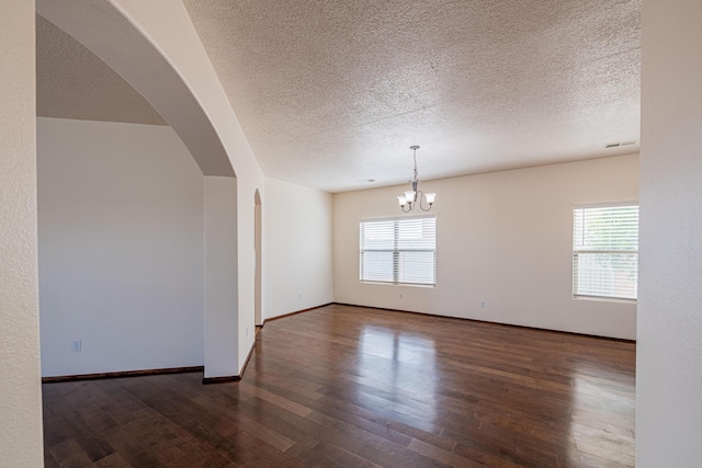 empty room with visible vents, a notable chandelier, wood finished floors, arched walkways, and baseboards