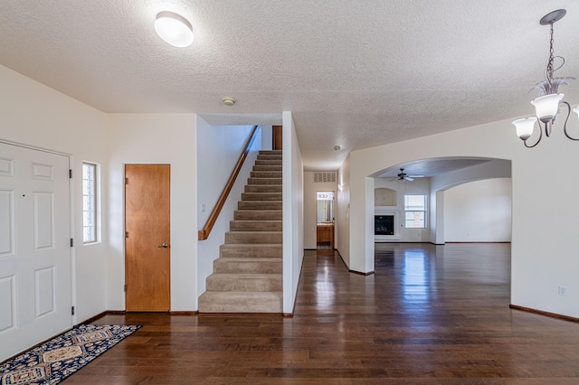 foyer entrance with stairway, wood finished floors, arched walkways, a textured ceiling, and a notable chandelier